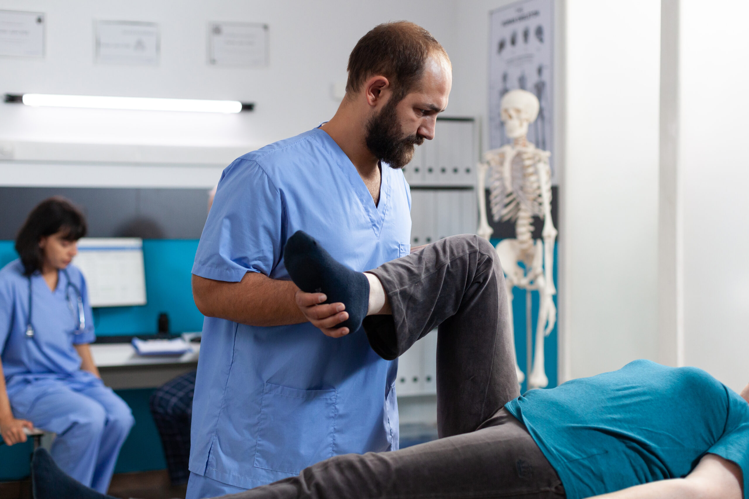Chiropractic physician helping aged woman with leg muscle pain Chiropractic physician helping aged woman with leg muscle pain in osteopathy cabinet. Orthopedic assistant treating patient with knee injury for physical recovery, giving support.